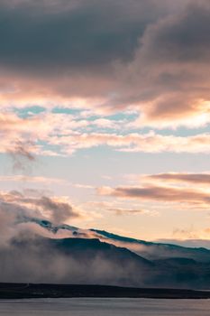 Capture of foggy mountains under a cloudy sky during golden hour, showcasing natural beauty and serene atmosphere.