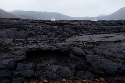 Free Captivating view of a rugged, cracked lava field with steam rising in the background, showcasing geological beauty. Stock Photo