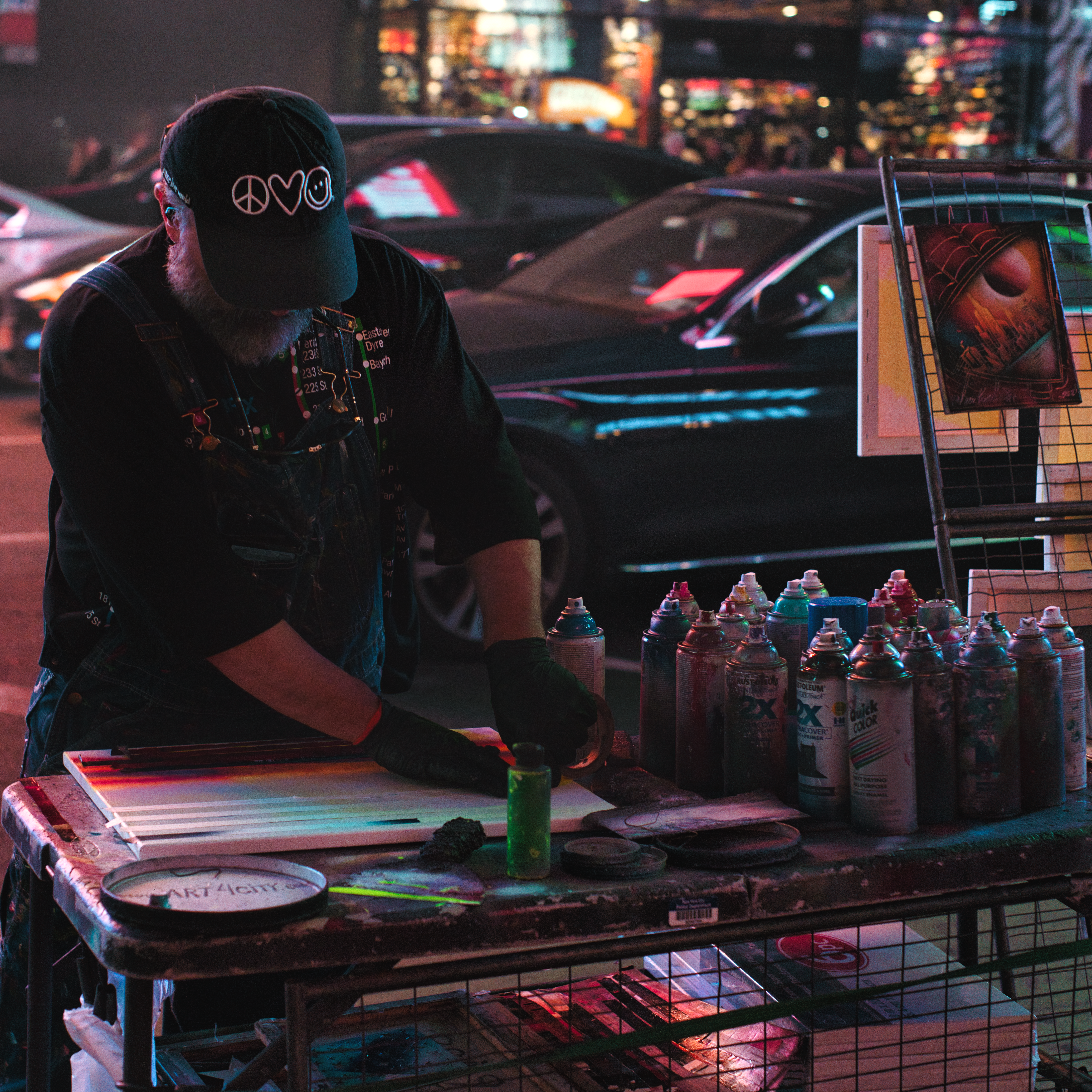 Street artist using spray paints to create artwork outdoors at night.