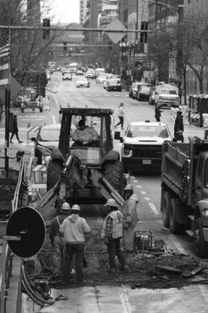 Monochrome image of workers and machinery on a busy city street.