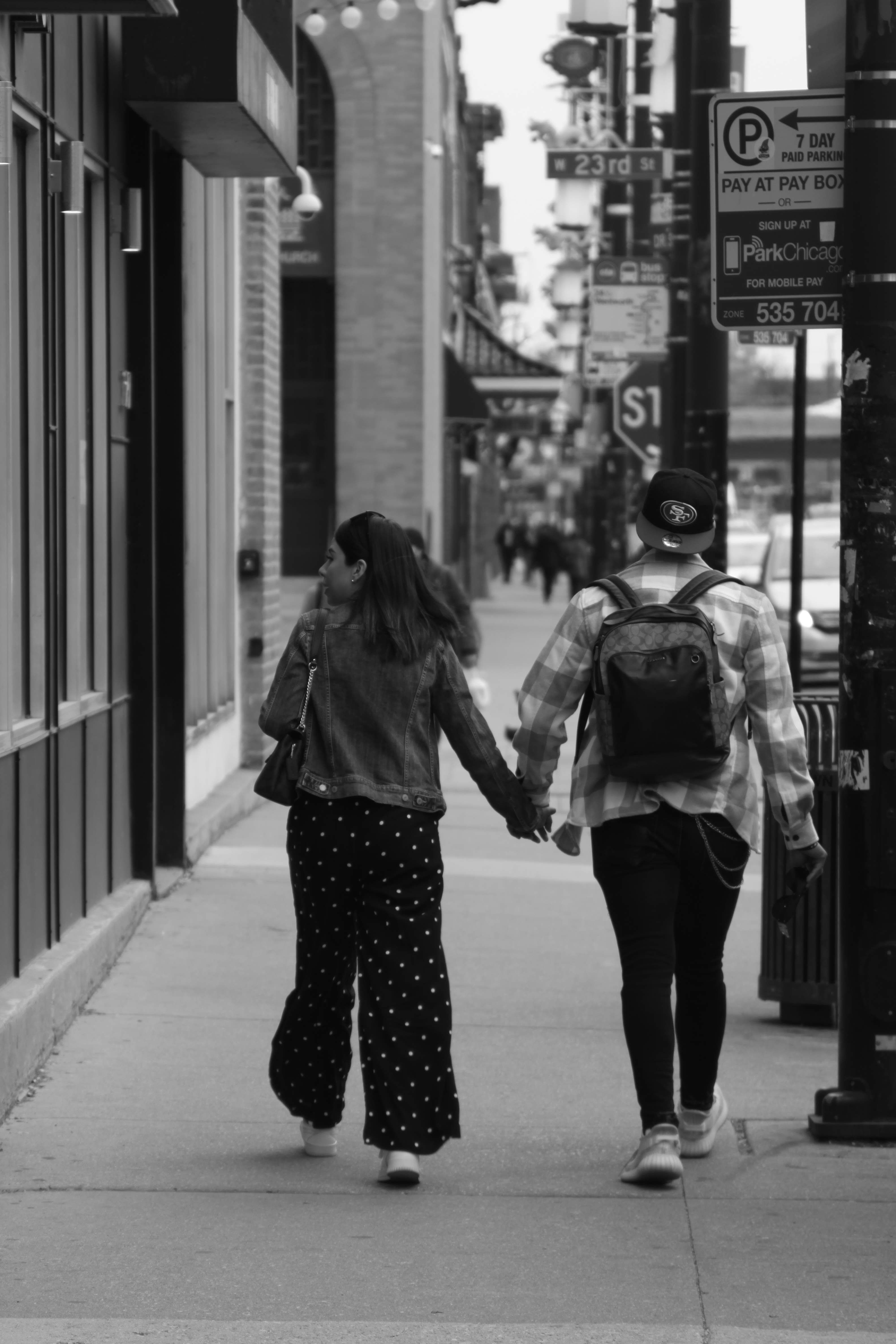 A couple walks hand in hand on a city sidewalk, captured in black and white for a timeless feel.