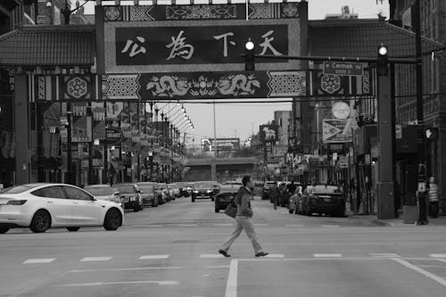 Grayscale Photo of Man Walking on the Pedestrian Lane