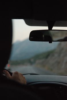 View from inside a car with a driver on a scenic mountain road during twilight.