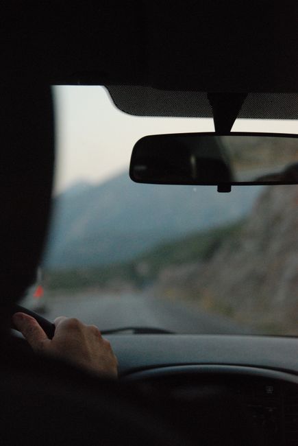 Fotomural Vista desde dentro de un coche con un conductor en una carretera de montaña escénica durante el crepúsculo.