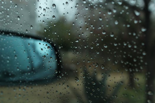 Close-up image of raindrops on a car window with rearview mirror reflection.