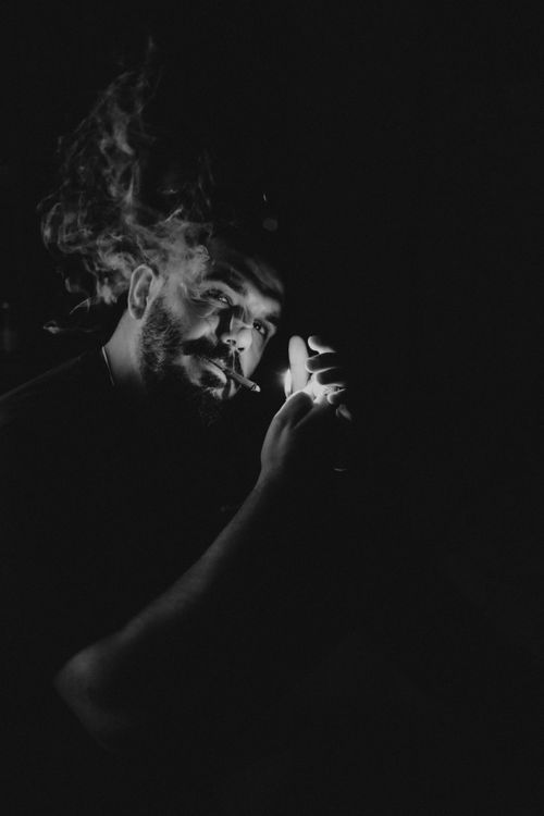Free Artistic black and white portrait capturing a man smoking in dramatic low light. Stock Photo