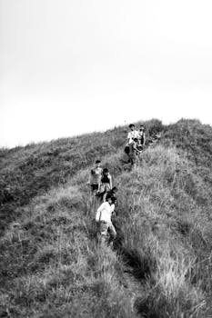 A group of people exploring a grassy hill in a monochrome landscape.