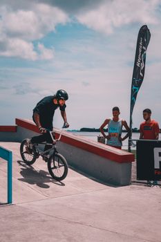A BMX rider performs a stunt on a skatepark ramp with onlookers nearby, capturing a dynamic outdoor scene.