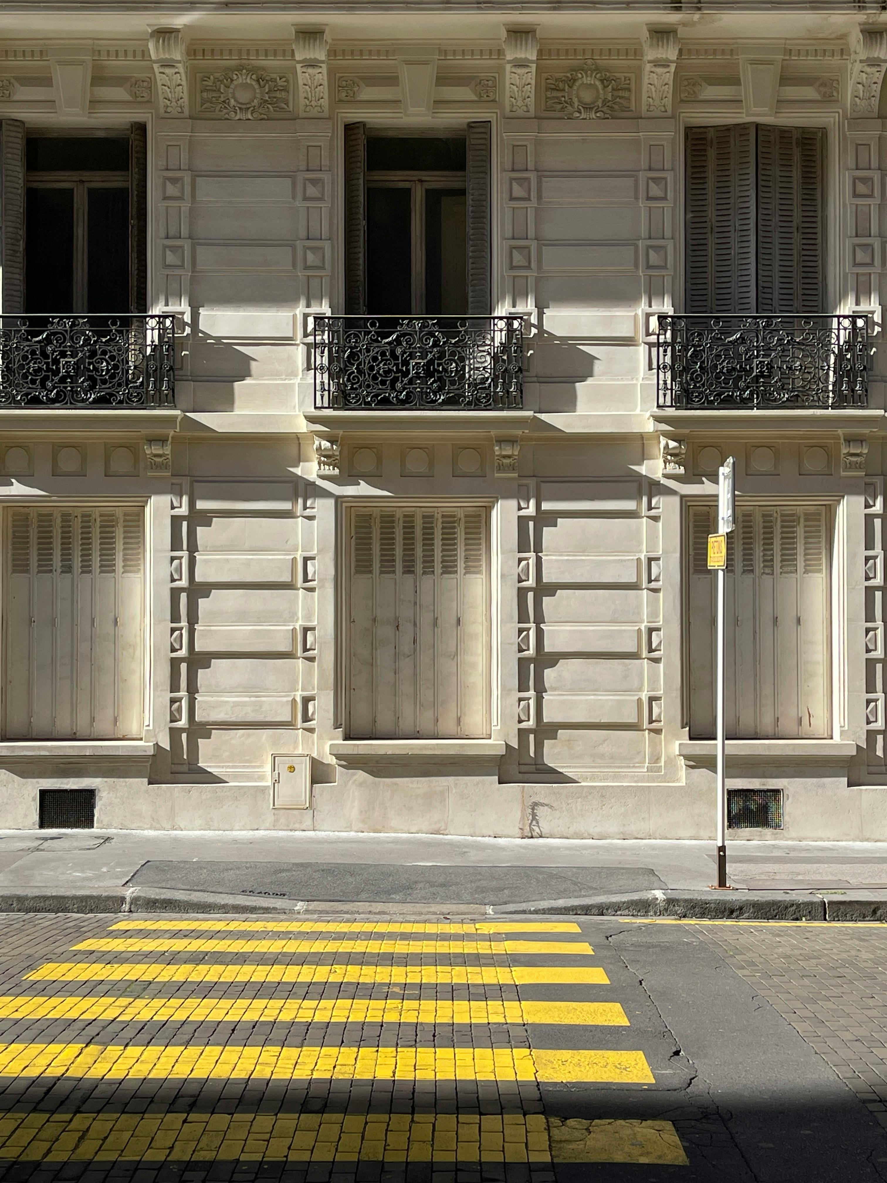 Street view of a Parisian building facade featuring balconies and a yellow pedestrian crosswalk.