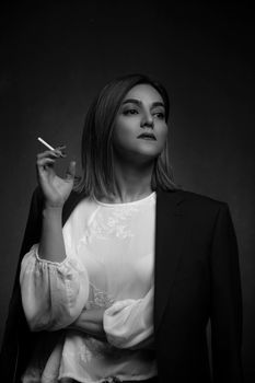 Black and white photo of a woman in a blazer holding a cigarette, exuding elegance.