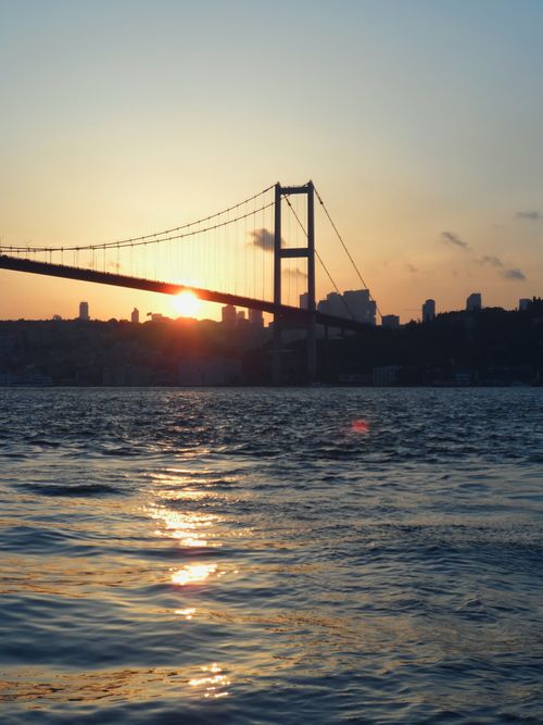 Free Golden hour at Bosphorus Bridge with sun setting over city skyline and ocean waves. Stock Photo