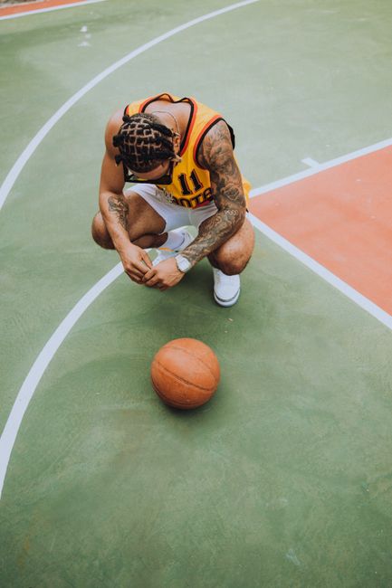 A man in a basketball jersey crouches on an outdoor court with a basketball.