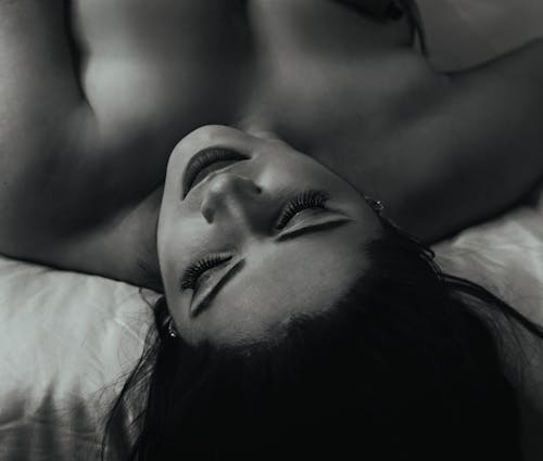 Grayscale Photo of a Topless Woman Lying on Bed