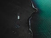 无人机在碧绿海浪下的黑色沙滩上拍摄了一辆汽车的照片