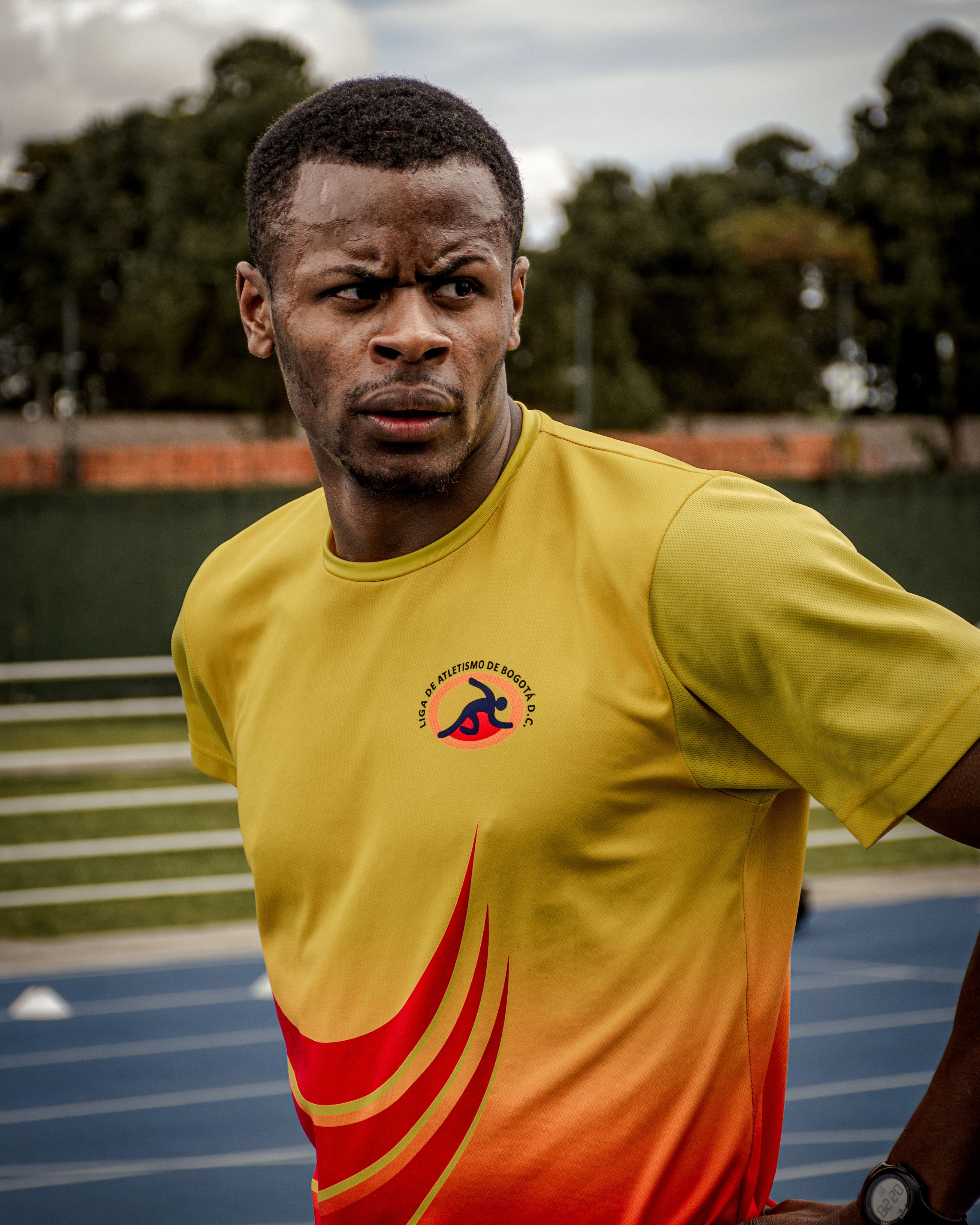 Focused African American male athlete in a yellow shirt on an outdoor track.