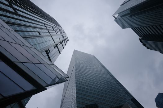 Low angle view of modern skyscrapers with glass facades reaching into an overcast sky, highlighting architectural innovation.