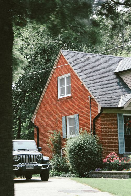 Free A picturesque brick house with a jeep parked in the driveway, surrounded by lush greenery. Stock Photo