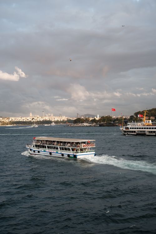 Free A scenic view of cruise boats on the Istanbul strait under a moody sky, featuring the city's skyline. Stock Photo