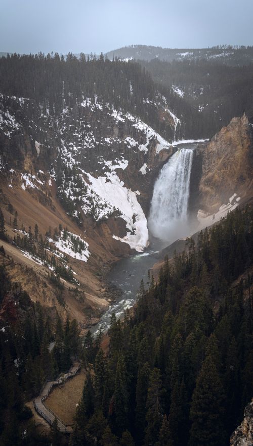 Free A breathtaking view of a snow-touched waterfall cascading through a lush forest in winter. Stock Photo