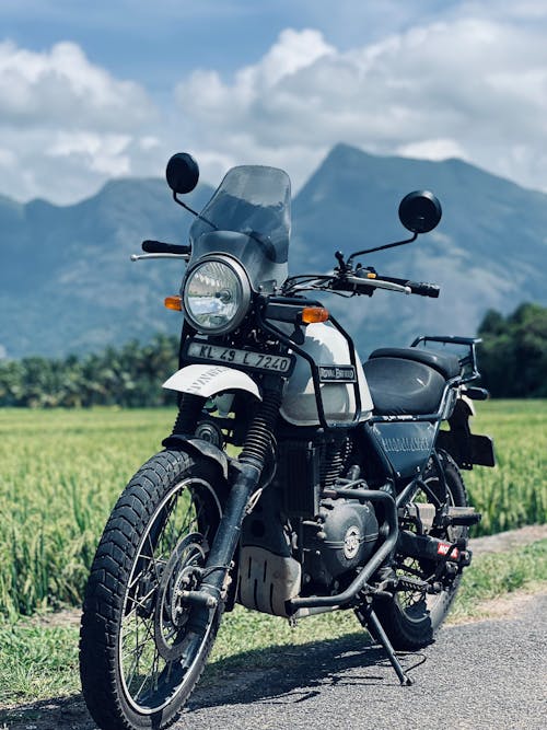 Black Motorcycle Parked Beside Grass Field Under Cloudy Sky
