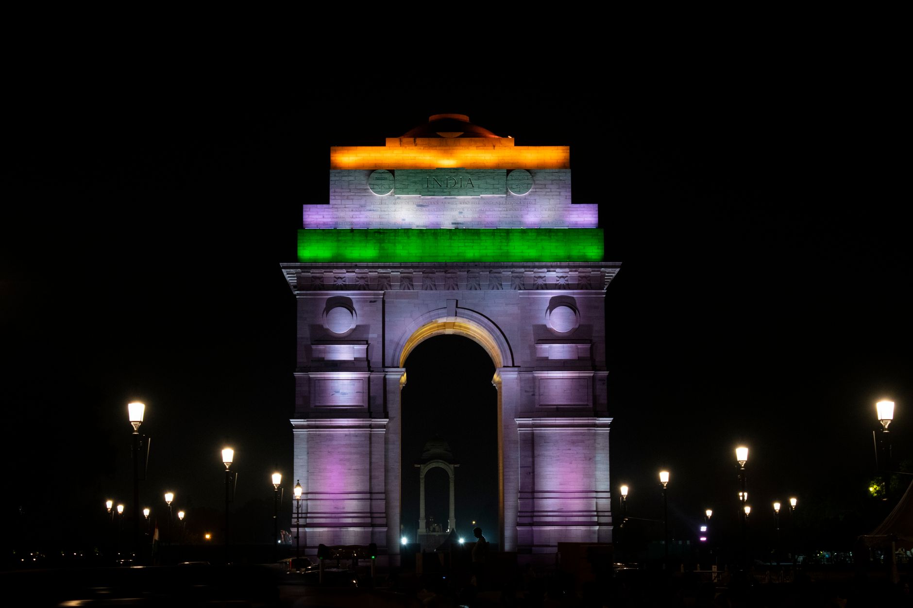 India Gate illuminated at dusk with visitors walking across New Delhi’s broad ceremonial avenue
