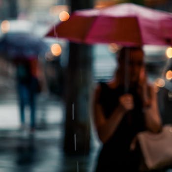 Blurred city scene with people holding umbrellas in the rain.