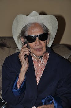 Senior woman with sunglasses and cowboy hat, smiling while talking on phone indoors.