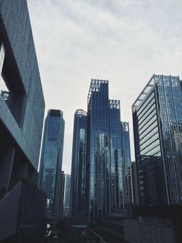 Low-angle shot of modern skyscrapers with glass facades against a cloudy sky.