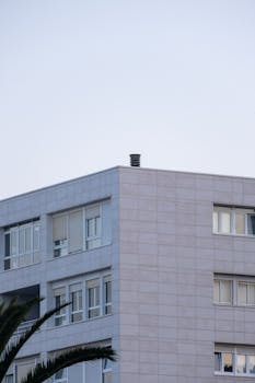 A modern urban residential building with palm trees set against a clear sky, showcasing contemporary architecture.
