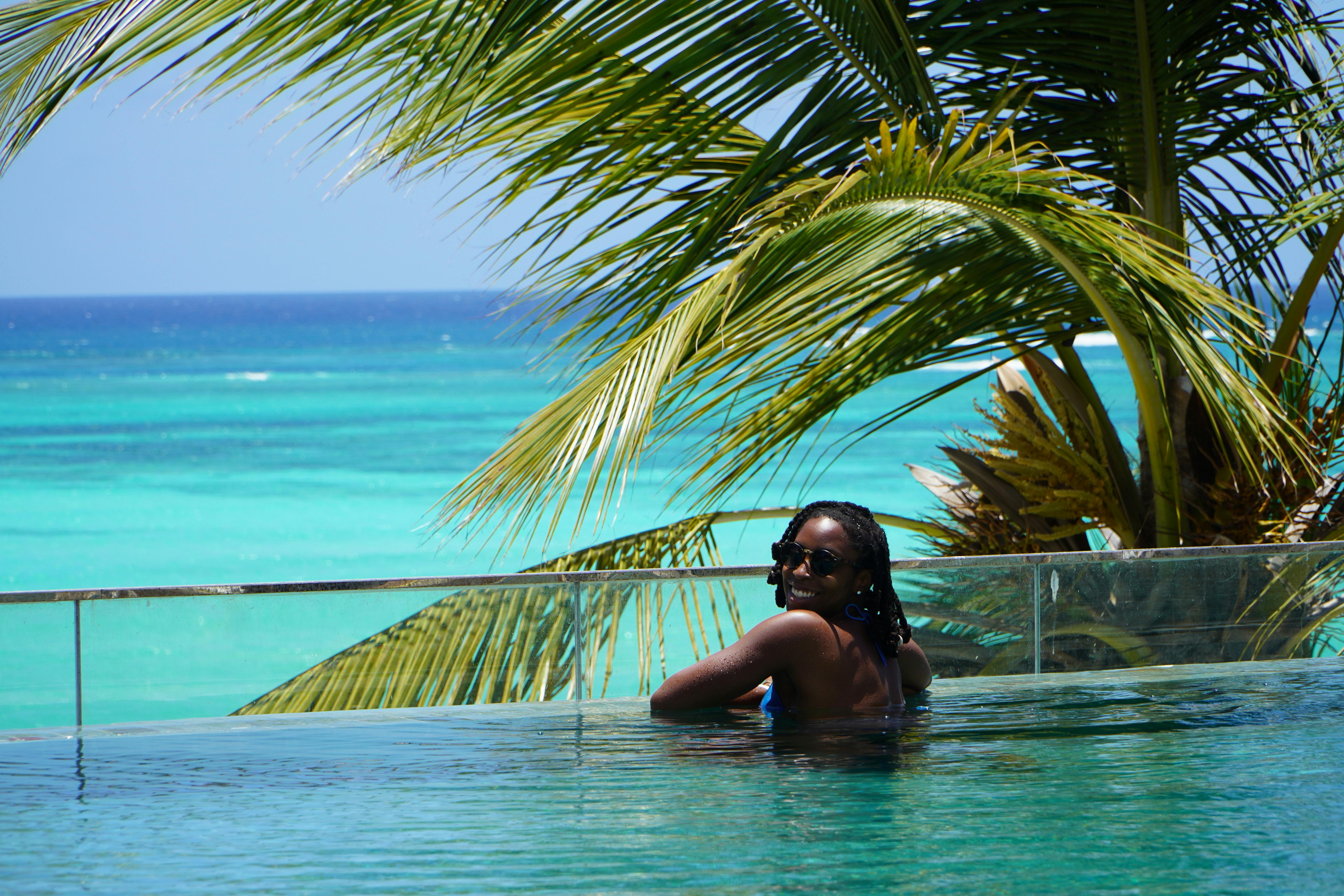 Woman enjoying a sunny day in an infinity pool with ocean view.