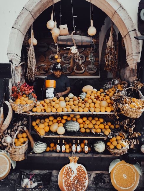 Colorful fruit stand with citrus and gourds at market archway.