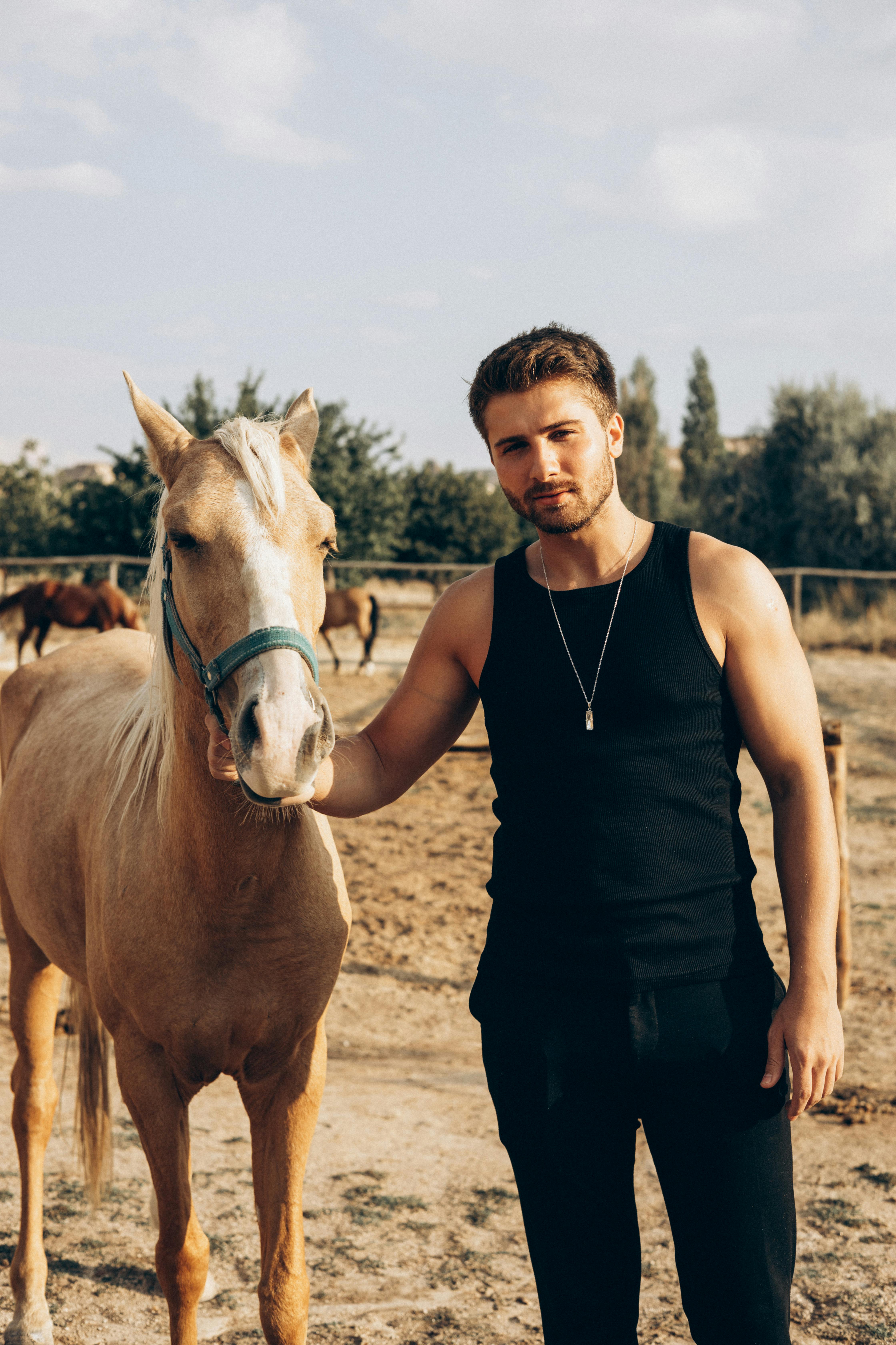 a man in black tank top holding brown horse