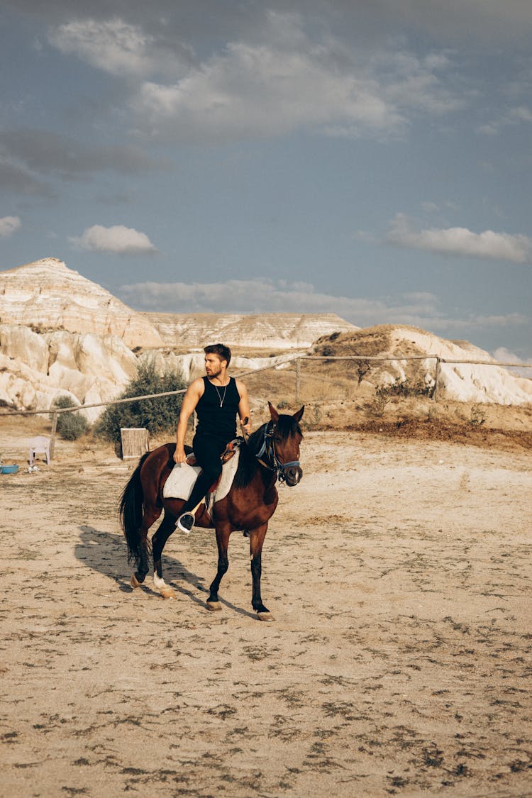 A Man In Black Tank Top Riding Brown Horse