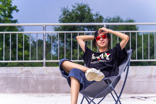 Woman in Black T-shirt and Blue Denim Shorts Sitting on Black Metal Chair