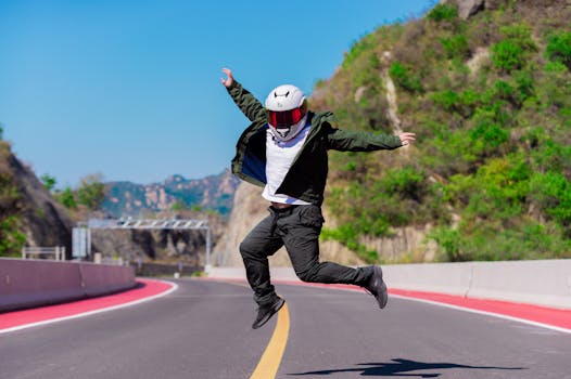 A person in a helmet jumps energetically on a scenic mountain road.