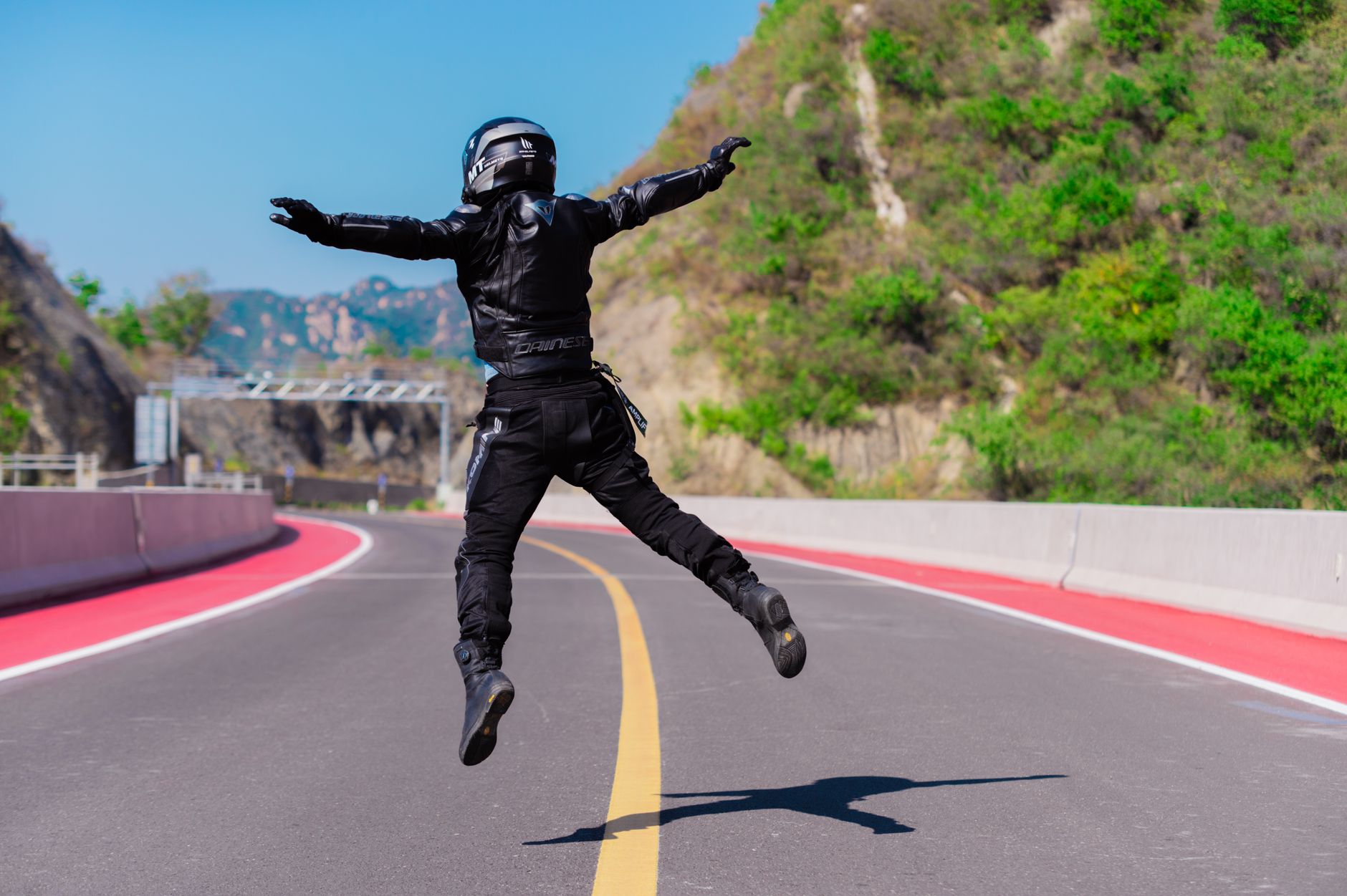 A motorcyclist in full gear jumps with joy on a scenic mountain road.