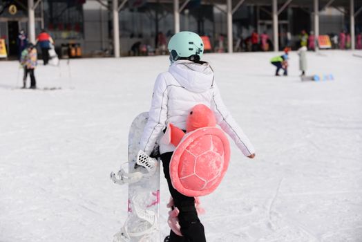 Woman with turtle backpack snowboarding on sunny winter day at ski resort.