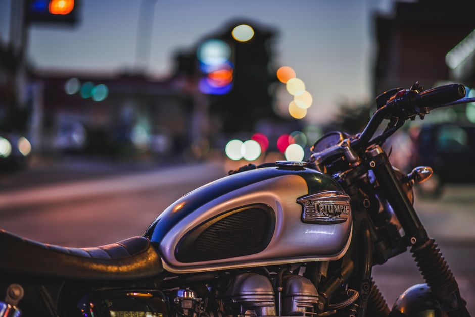 Dynamic close-up of a Triumph motorcycle parked on an illuminated city street at dusk.