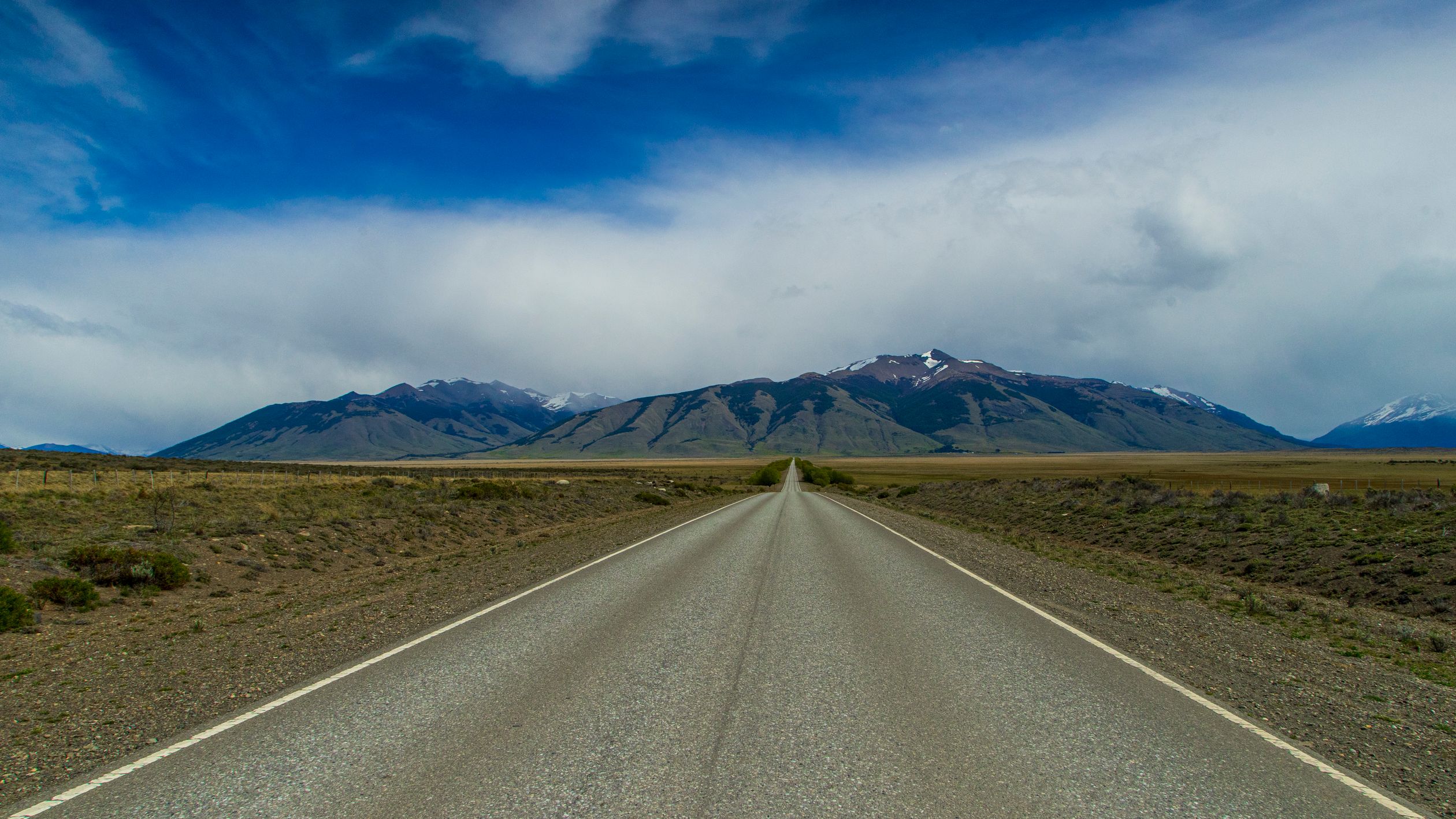Straight road leading through Patagonian Andes under dramatic sky in Perito Moreno, Argentina.