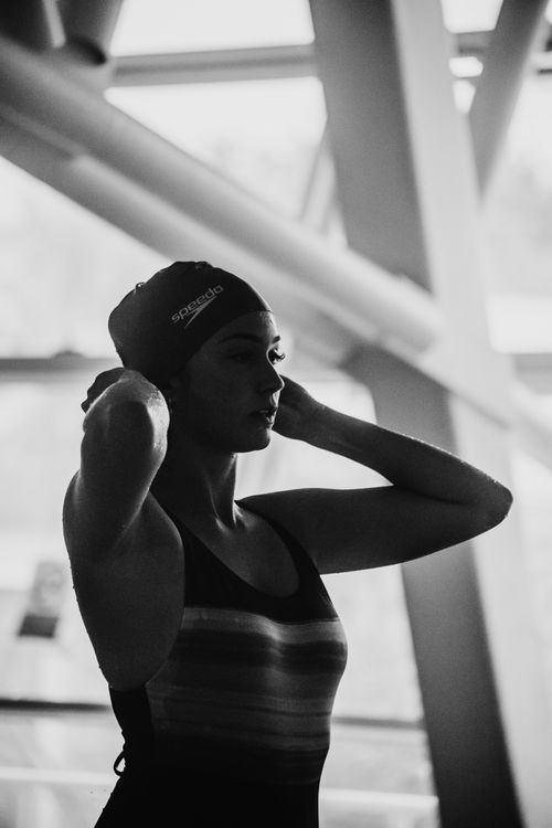 Free Black and white image of a female swimmer adjusting her cap indoors. Stock Photo
