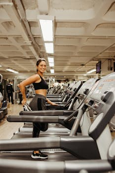 Smiling woman stretching on a treadmill in a gym setting, promoting a healthy lifestyle.