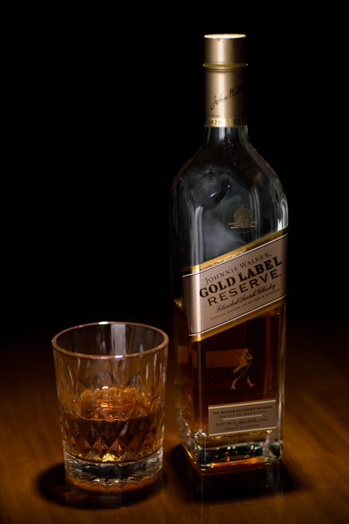 Free A classy setup of a whiskey bottle and glass on a wooden surface with dark background. Stock Photo