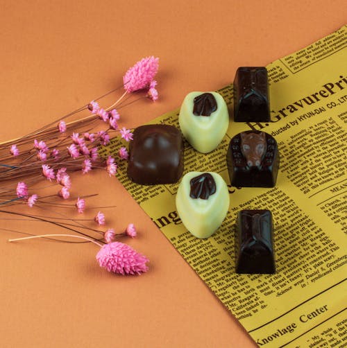Free Chocolate Pralines on Newspaper Next to Pink Flowers Stock Photo