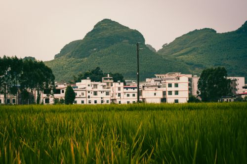 Free Picturesque village by lush green fields and mountains under a clear sky. Stock Photo