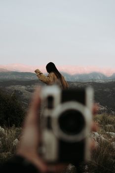 Woman enjoys adventure in mountains with vintage camera foreground, showcasing travel and exploration spirit.