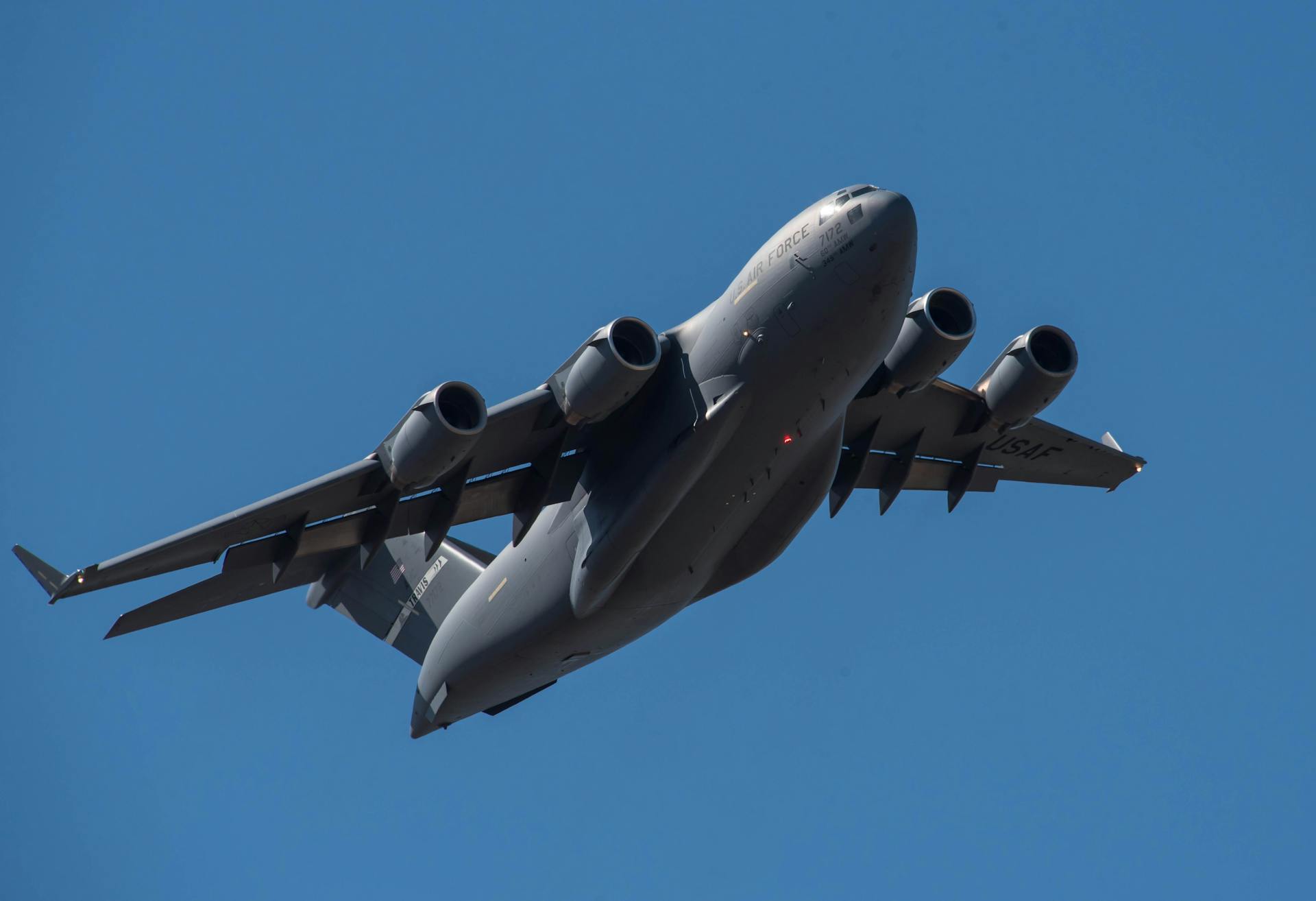 A military aircraft flying high against a clear blue sky, showcasing aviation technology.