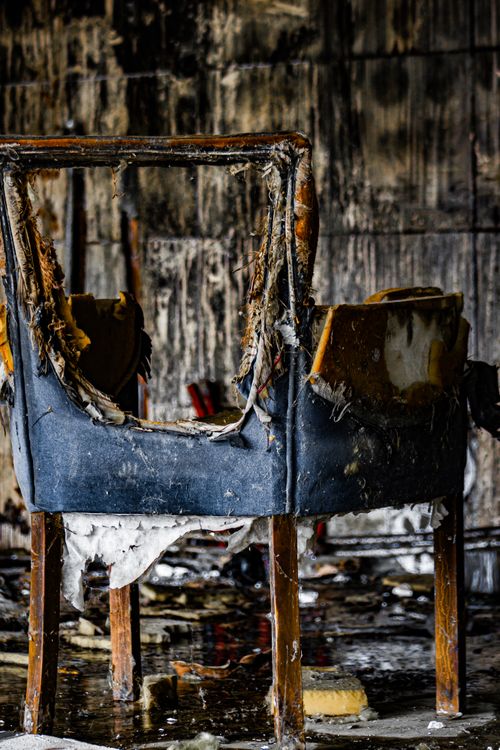 Free A worn, burnt chair in an old, abandoned room with peeling walls. Stock Photo
