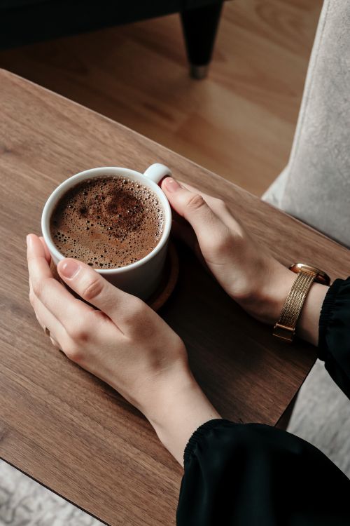 Free High angle view of hands holding a warm cup of coffee on a wooden table. Stock Photo