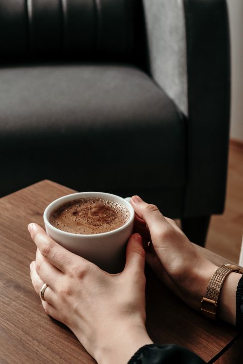 Free Cozy scene of hands holding a warm coffee cup on a wooden table indoors. Stock Photo