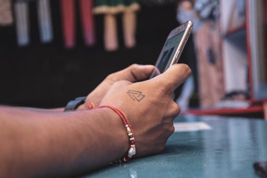 Detailed view of a hand with a tattoo holding a smartphone indoors, showcasing modern technology.